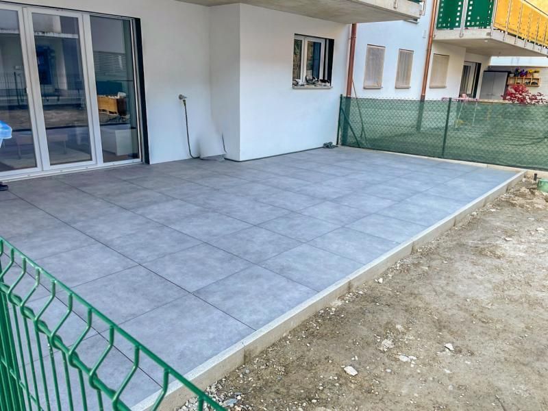 Un patio avec une clôture verte et un bâtiment blanc en arrière-plan