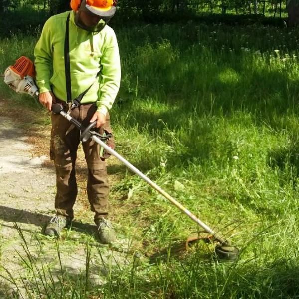 Un homme portant un casque coupe l'herbe avec une tondeuse
