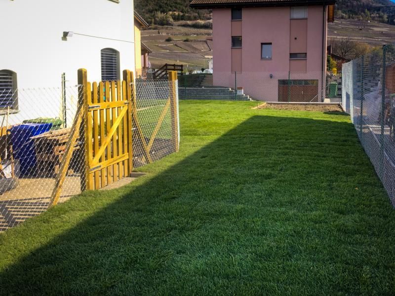 Une cour clôturée avec un portail et un bâtiment rose en arrière-plan