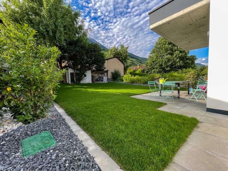 Une pelouse verte luxuriante avec une table et des chaises dans l'arrière-cour d'une maison.