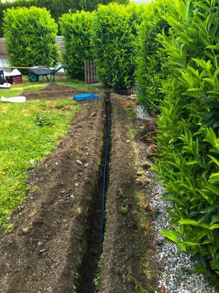 Une tranchée dans le sol dans un jardin avec une brouette en arrière-plan.