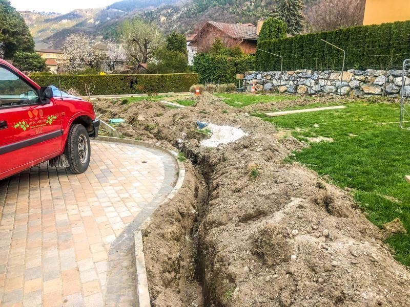 Une voiture rouge est garée dans une allée à côté d'un gros tas de terre.