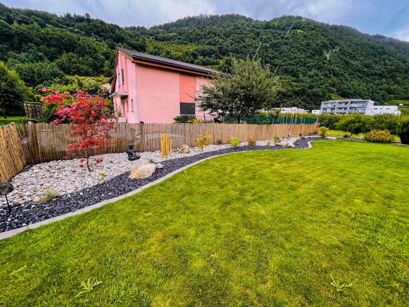 Une grande pelouse verte luxuriante avec une maison rose en arrière-plan.