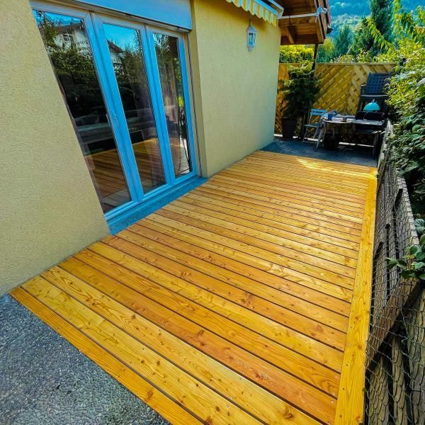 Une terrasse en bois devant un bâtiment jaune