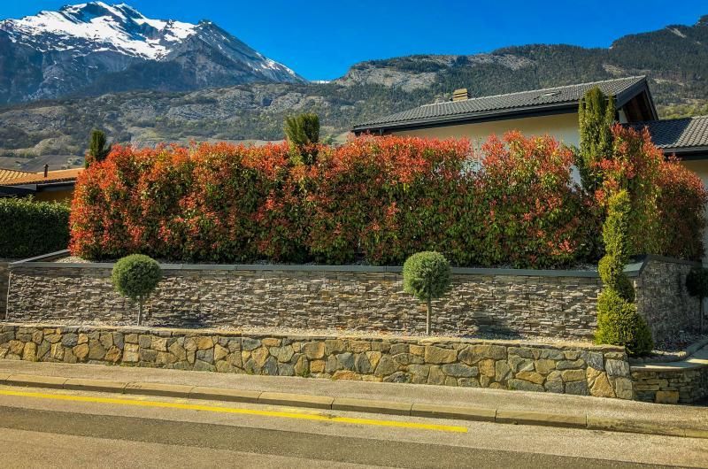 Un mur de pierre entoure une maison avec des montagnes en arrière-plan.