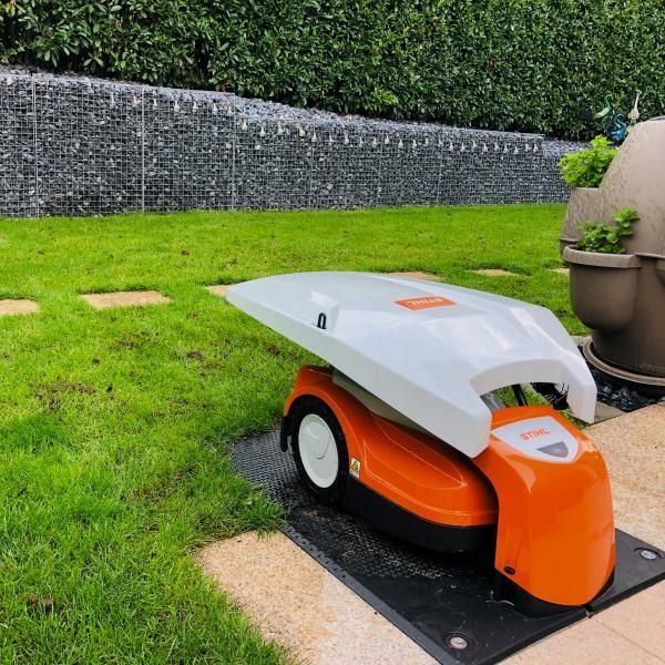 Une tondeuse à gazon robotisée orange et blanche est garée sur une terrasse