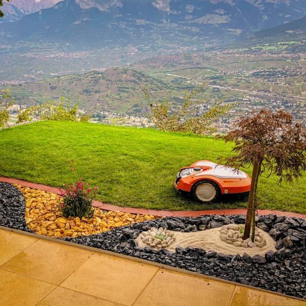 Une tondeuse à gazon robotisée est posée au sommet d'une colline verdoyante.