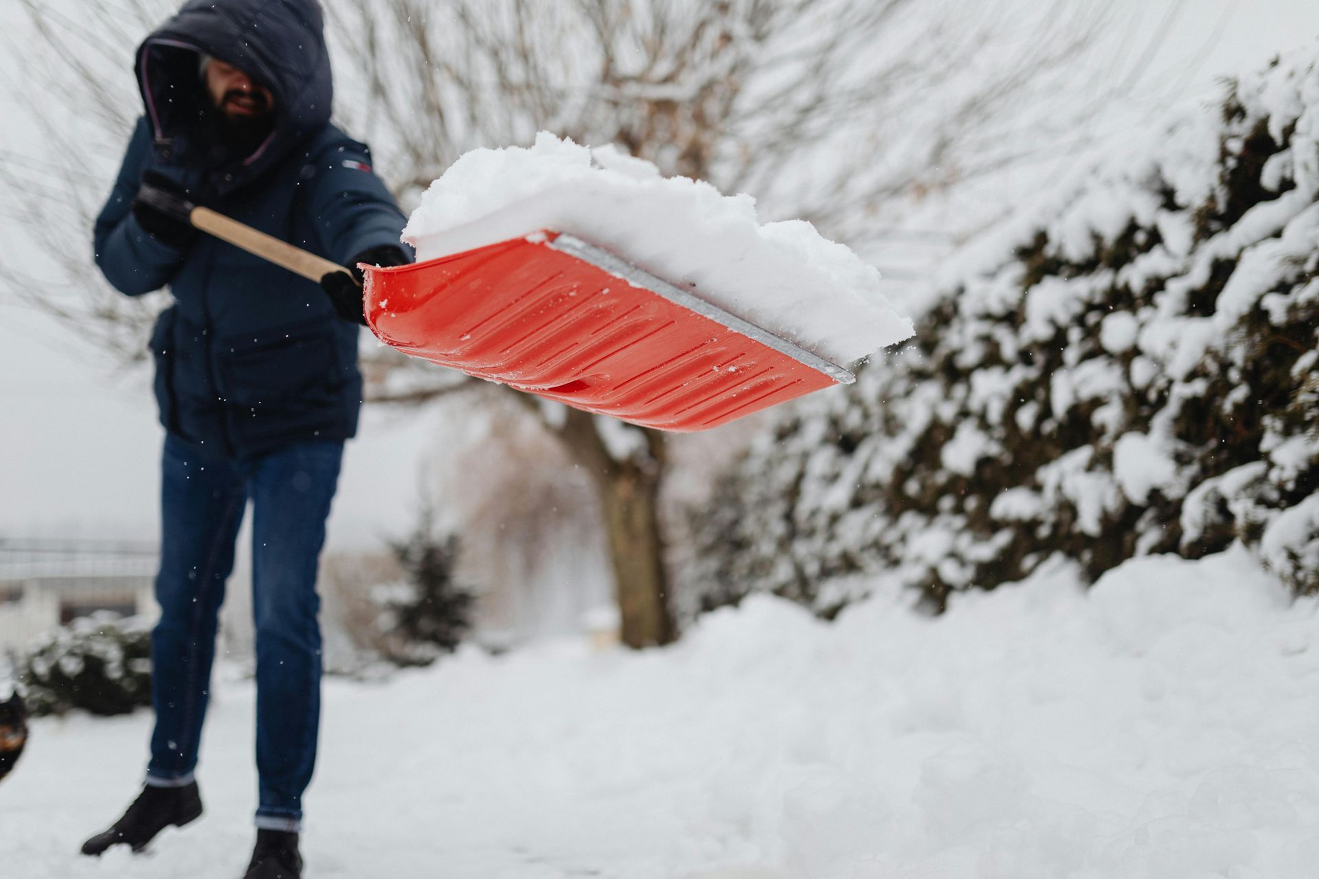 Un homme pellette la neige du trottoir avec une pelle rouge.