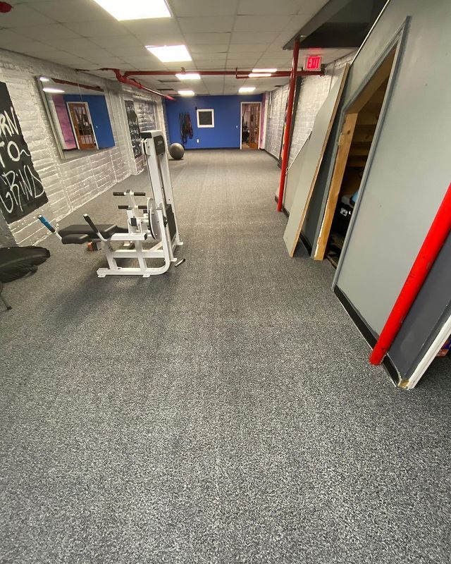 A gym with a gray carpeted floor and a row of exercise equipment.