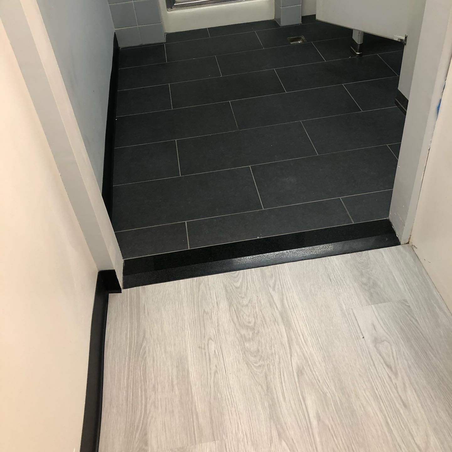 A bathroom with a black tile floor and a white wood floor.