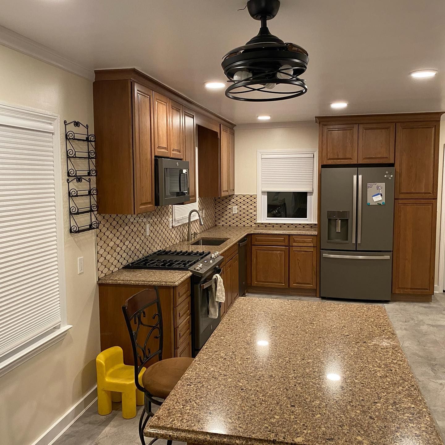 A kitchen with wooden cabinets , granite counter tops , a refrigerator and a ceiling fan.