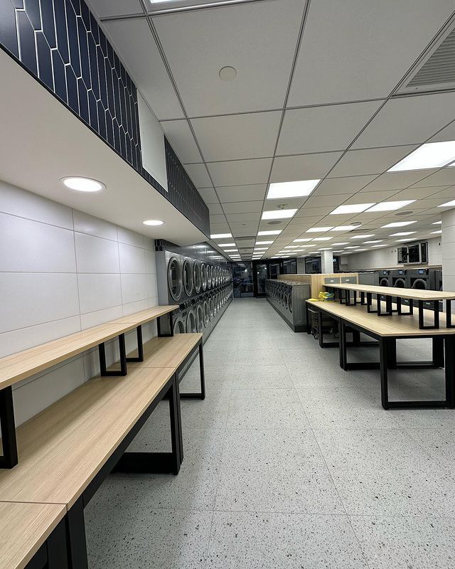 A long hallway in a laundromat with tables and benches.