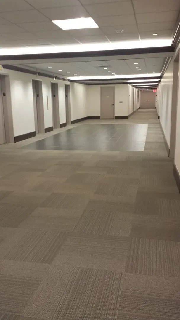 An empty hallway with a carpeted floor and a red exit sign