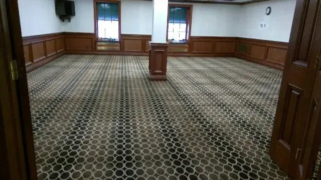 An empty room with a patterned carpet and wood paneling