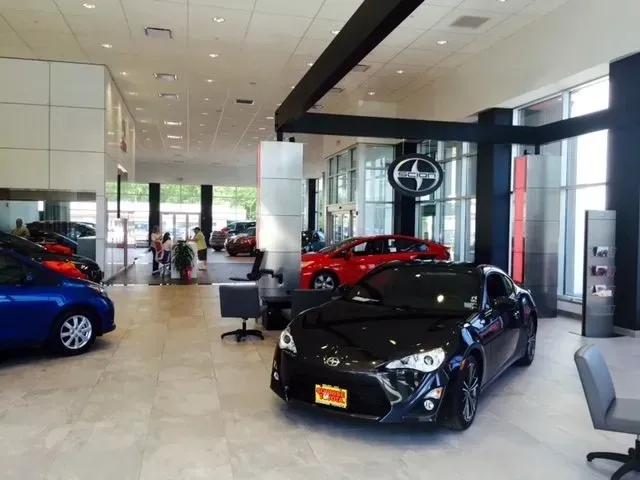 A black car is parked in a showroom with other cars