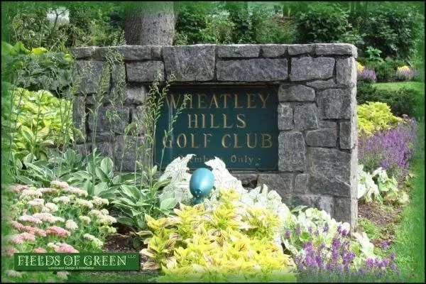 A sign for meatley hills golf club is surrounded by flowers