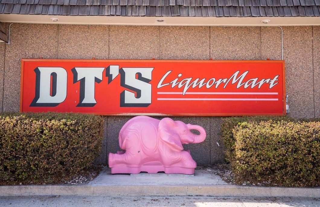 A pink elephant is in front of a red sign for dt 's liquor mart