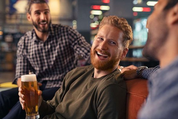 A group of men are sitting on a couch drinking beer and laughing.