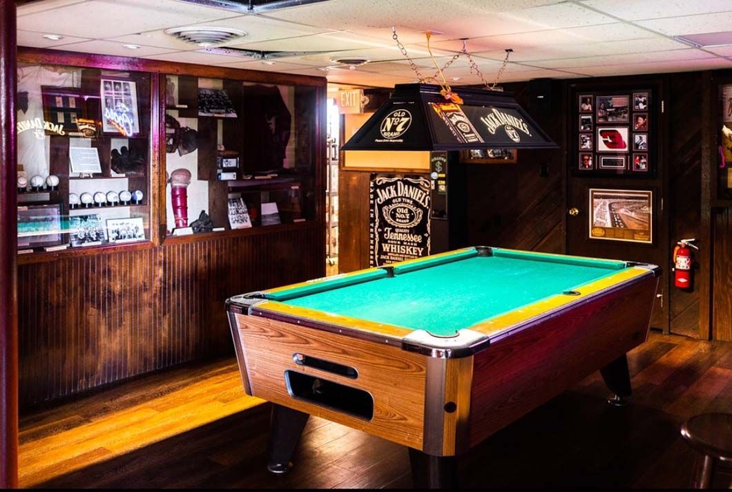 A pool table in a bar with a jack daniels sign on the wall