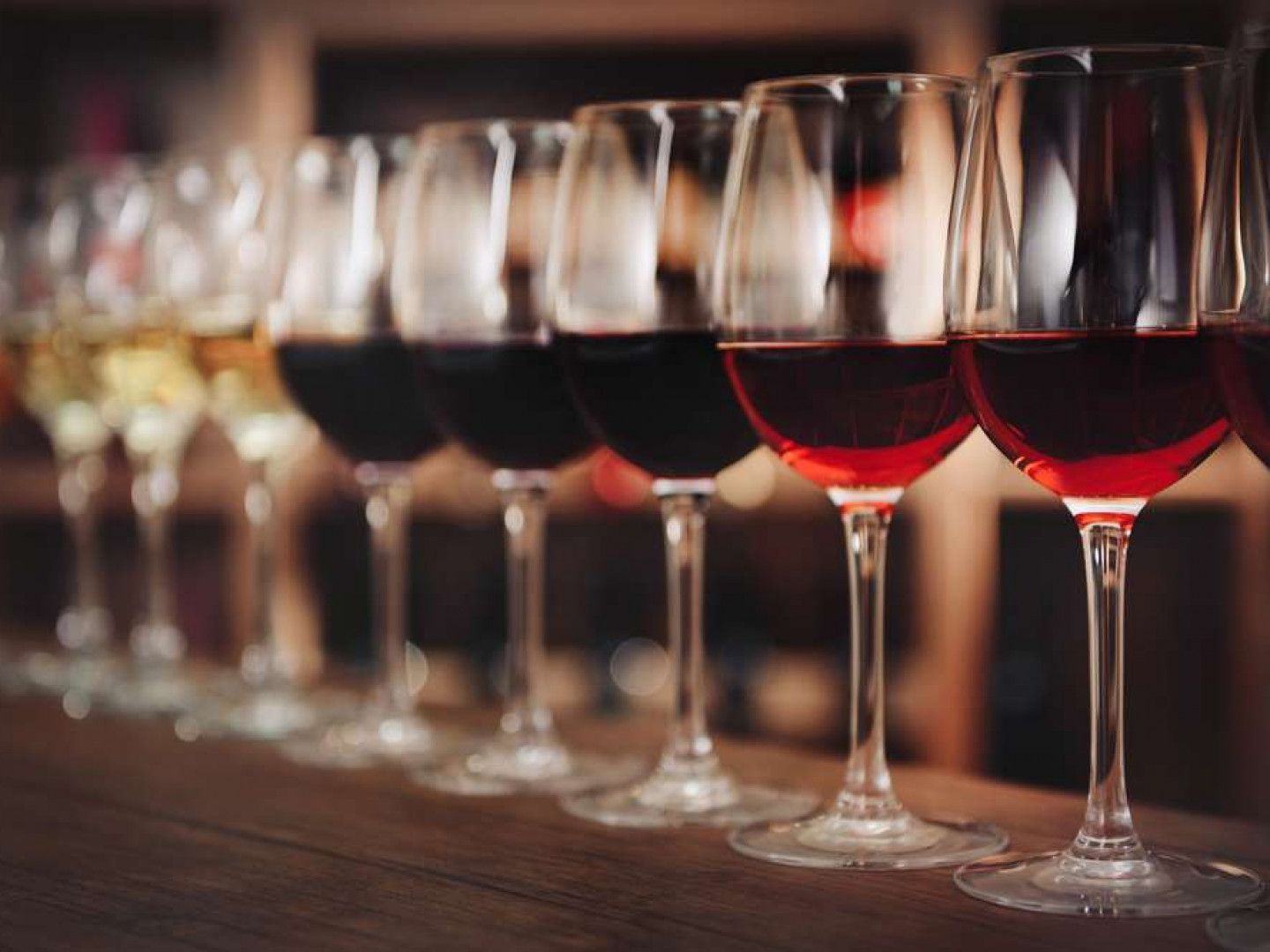 A row of wine glasses filled with different types of wine on a table.