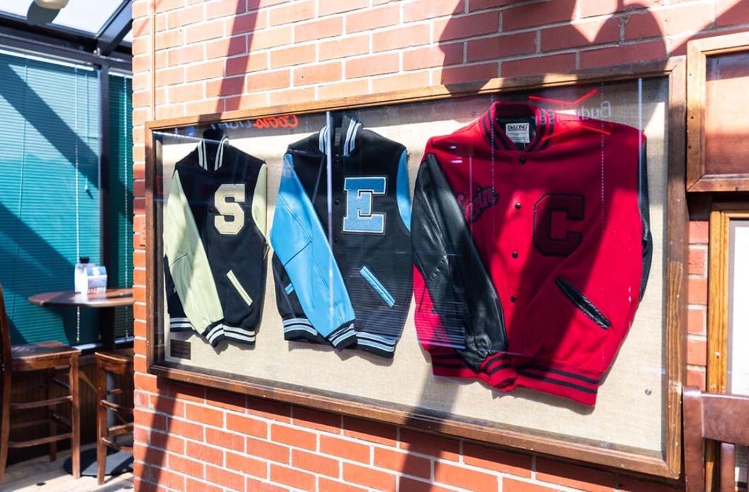 Three varsity jackets are hanging on a brick wall.