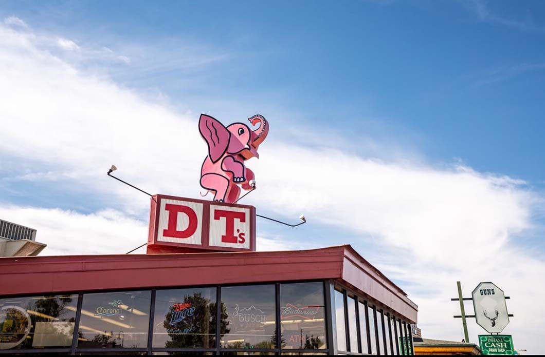 A pink elephant is sitting on top of a building with the word dt on it.
