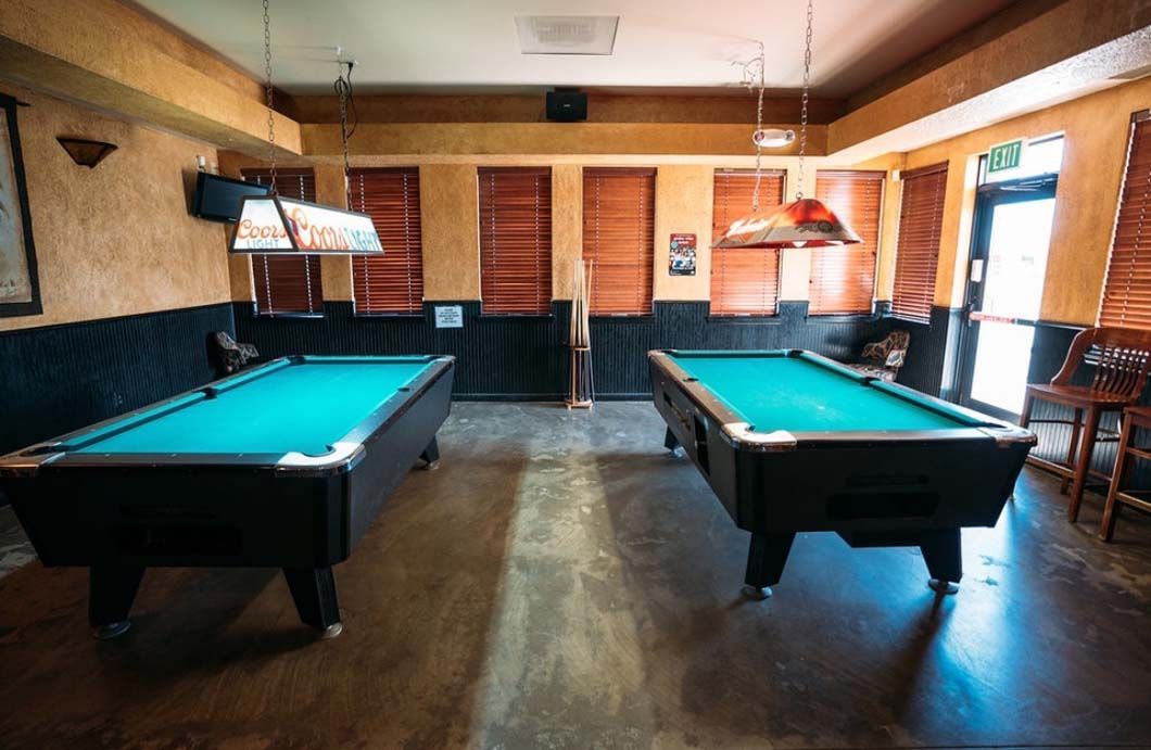 Two pool tables are in a room in a bar.