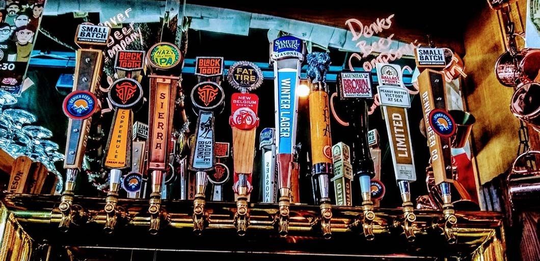 A bunch of beer taps are lined up on a bar.
