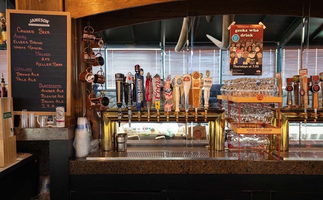 A bar with a lot of beer taps and a menu on the wall.