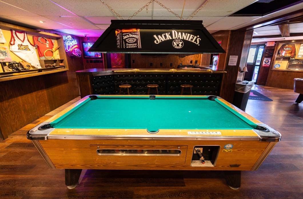 A pool table in a bar with a jack daniels sign above it.