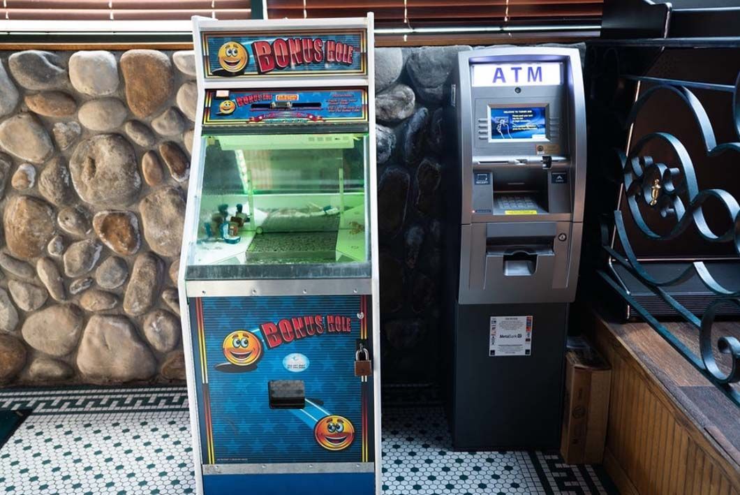 An arcade machine and an atm machine are sitting next to each other in a room.