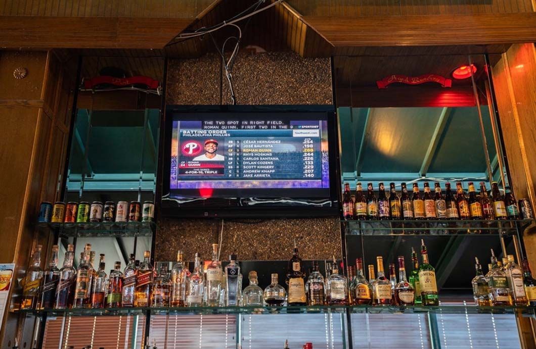 A bar with a television on the wall and bottles of alcohol on the shelves.