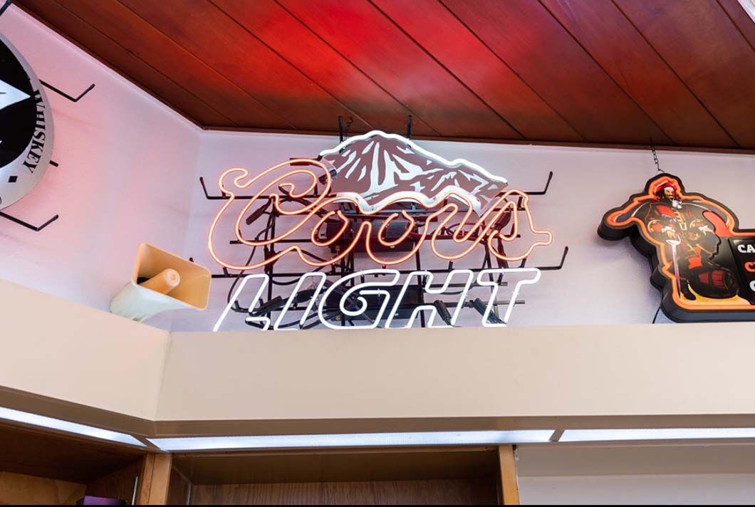 A neon sign for coors light hangs from the ceiling