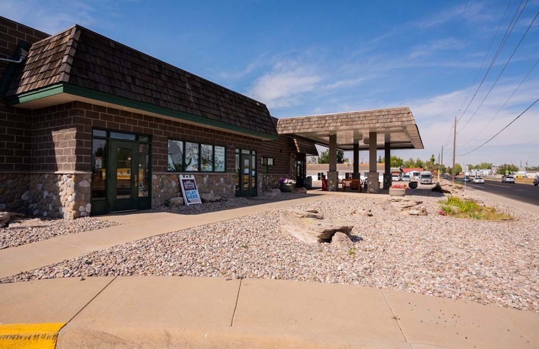 A brick building with a green roof is sitting next to a gravel road.