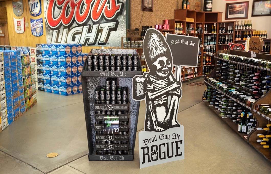 A store filled with lots of beer bottles and a cardboard cutout of a skeleton holding a sign.