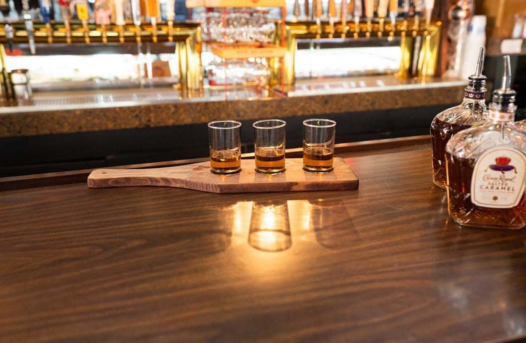 A bar with three shot glasses and a bottle of whiskey on it.