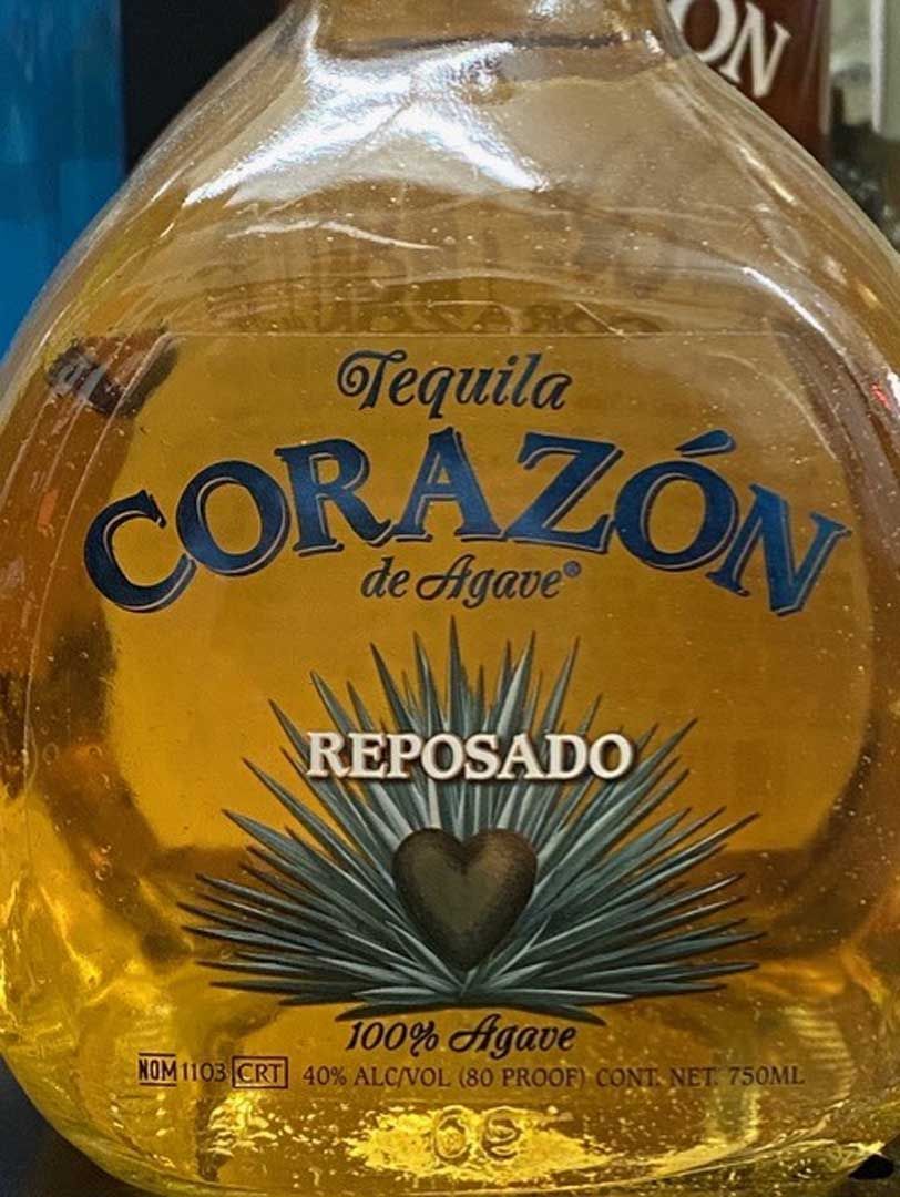 A bottle of tequila corazón de agave reposado is sitting on a table.
