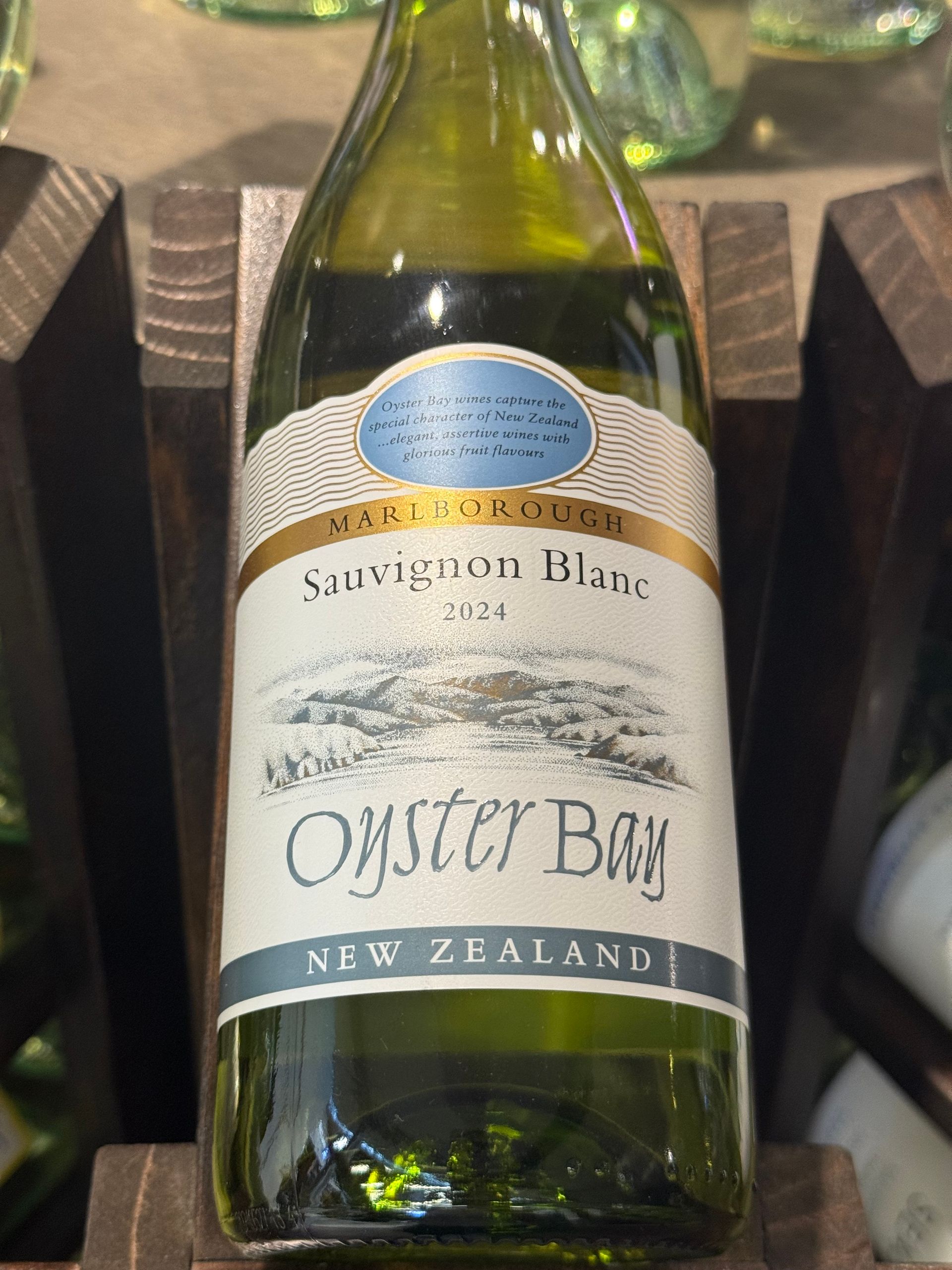 Bottle of Oyster Bay Sauvignon Blanc wine. White label with blue and gold accents, against a wooden rack.