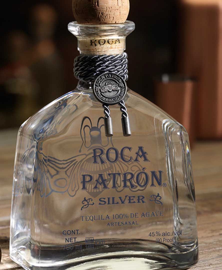 A bottle of roca patron silver tequila is sitting on a wooden table.