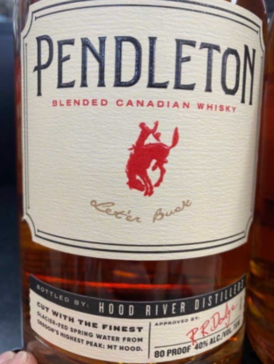 A person is holding a bottle of pendleton blended canadian whisky