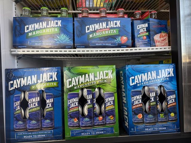 Cayman Jack margarita drinks in display. Boxes and cans in various flavors: margarita, strawberry, and mixed citrus.