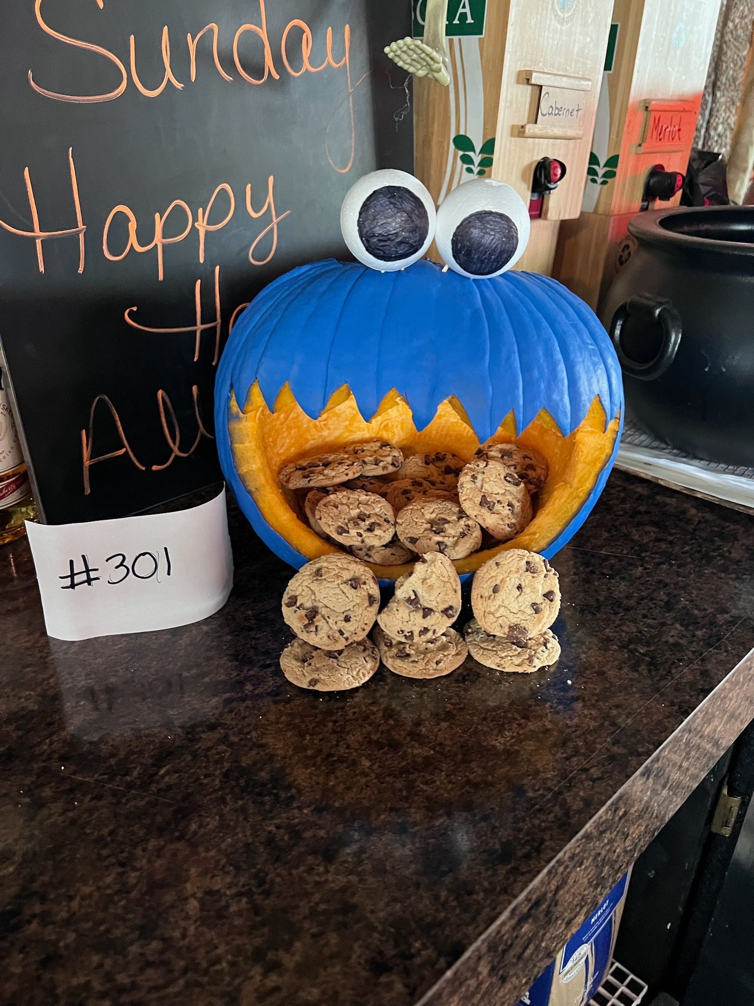 A cookie monster pumpkin filled with chocolate chip cookies on a counter.