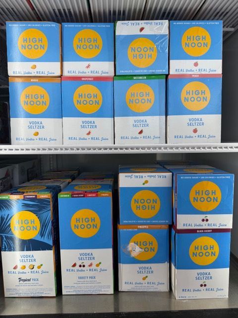 Shelves stocked with High Noon hard seltzer boxes, various flavors with a blue and yellow design.