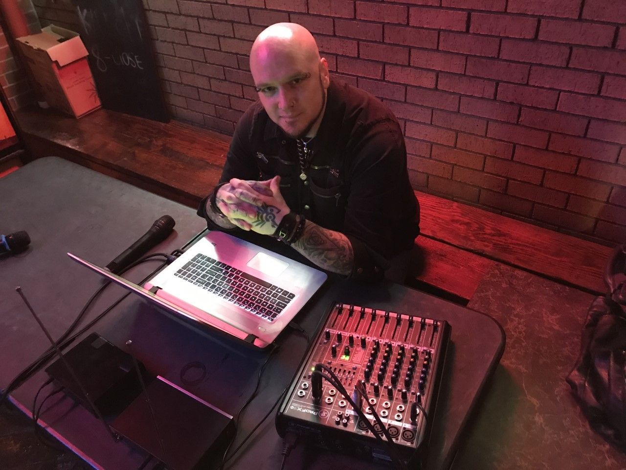 A bald man is sitting at a table with a laptop and a microphone