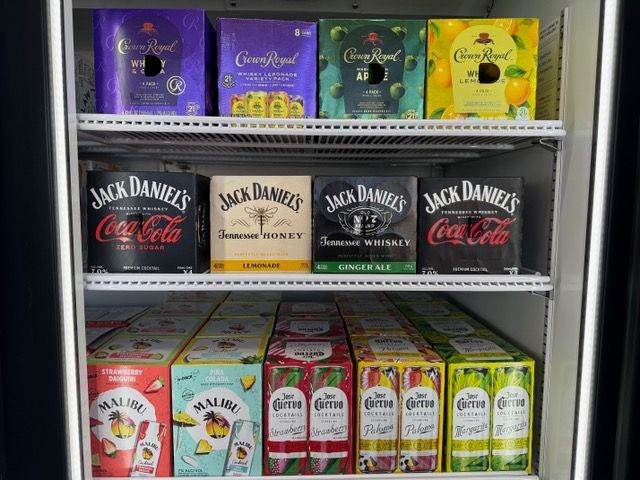 A cooler stocked with various alcoholic beverages, including Crown Royal, Jack Daniel's, and Malibu, and Corona cocktails.