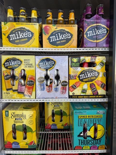 Shelves of Mike's Hard Lemonade and other flavors in a refrigerator; yellow, orange, and purple boxes.