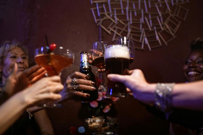 A group of people are toasting with drinks at a bar.