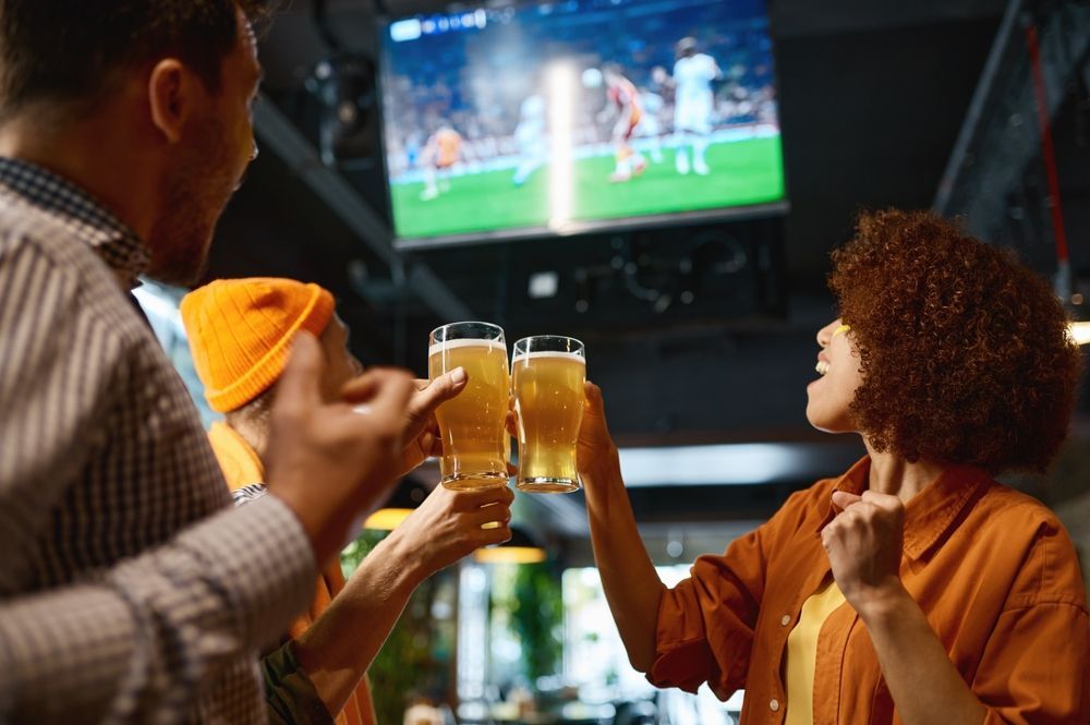 A group of people are toasting with beer in a bar while watching a soccer game.