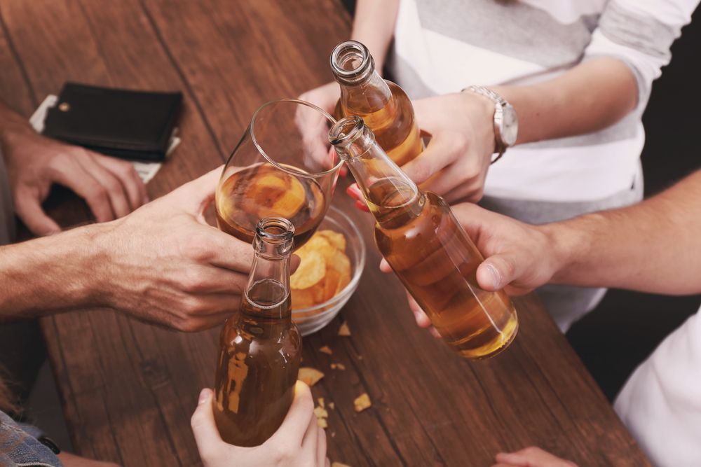 A group of people are toasting with beer bottles on a wooden table.