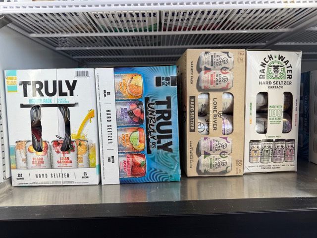 Four hard seltzer boxes on a shelf: Truly, Truly Uncaged, Loverboy, and Ranch Water.